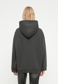 Haut à capuche surdimensionné gris foncé avec une grande capuche, coupe ample et ourlet côtelé. Texture de tissu douce et design minimaliste.