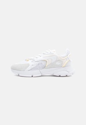 Fehér sneaker szürke velúr és hálós panelekből, texturált talppal, fűzős kialakítással és diszkrét, szürke és sárga logóelemekkel.