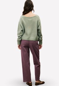 Grüner Strickpullover mit weitem Ausschnitt, kombiniert mit lockeren, lila Cordhosen. Das Outfit hat gerippte Bündchen und einen elastischen Bund.