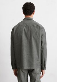 Gray industrial-style jacket with a smooth texture, featuring a collared neckline and buttoned cuffs. Tailored with a relaxed fit.