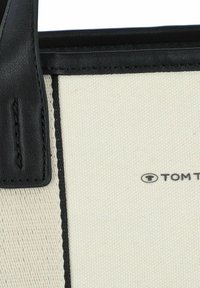 Borsa tote in tela con accenti in pelle nera. Corpo crema, cuciture nere e dettaglio del logo nell'angolo inferiore. Forma rettangolare con manici robusti.