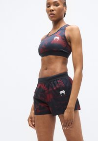 Ensemble brassière de sport et short noirs avec motifs abstraits rouges. Présente une coupe ajustée, une ceinture élastique et des détails de logo sur le tissu.