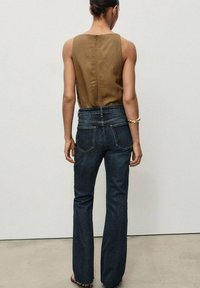 Top marrón sin mangas con cremallera en la parte posterior, combinado con jeans acampanados de color azul oscuro que tienen bolsillos traseros y dobladillos deshilachados.