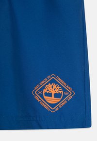 Modrá bavlnená tričká so svetložltou logom Timberland, diamantový tvar s dizajnom stromu a textom "EST. SINCE 73" pri leme.