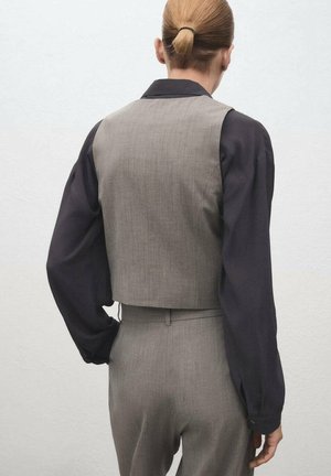 Gilet grigio a maniche corte realizzato in tessuto testurizzato, abbinato a una camicia nera a maniche lunghe. Include un colletto e una vita sagomata.