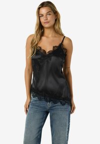 Mustast satiinist kamisol pitsist äärisega, varustatud reguleeritavate spagetirihmade ja lainelise äärega. Ühitatud helesiniste teksadega.