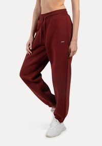Burgunderfarbene Sweatpants aus weichem, dehnbarem Stoff, mit elastischem Taillenbund, Kordelzug und gerippten Bündchen. Slim-Fit-Design mit Taschen an den Seiten.