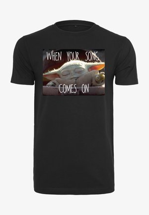 Musta puuvillainen t-paita, jossa on painettu kuva nukkuvasta hahmosta ja teksti "KUN LAULUSI SOI." Lyhyet hihat ja pyöreä pääntie.