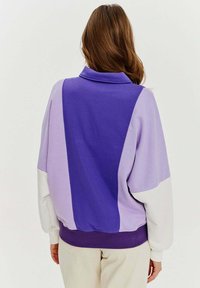 Fioletowy i lawendowy, oversize'owy hoodie z kołnierzem, z kolorowym blokiem i białymi akcentami. Miękka tkanina o luźnym kroju.