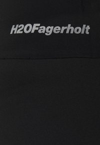 Tissu de sport noir avec une texture côtelée. Marque "H2O Fagerholt" en argent réfléchissant située près du bord supérieur.