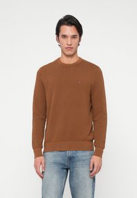 Brauner gestrickter Pullover mit Rundhalsausschnitt, langen Ärmeln und gerippten Bündchen. Verfügt über ein kleines Logo-Detail auf der Brust und einen strukturierten Stoff.