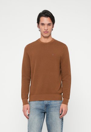 Pruun kootud kampsun, ümmarguse kaeluse, pikkade varrukate ja soonikkoes. Rinnal on väike logo ning kangas on tekstureeritud.