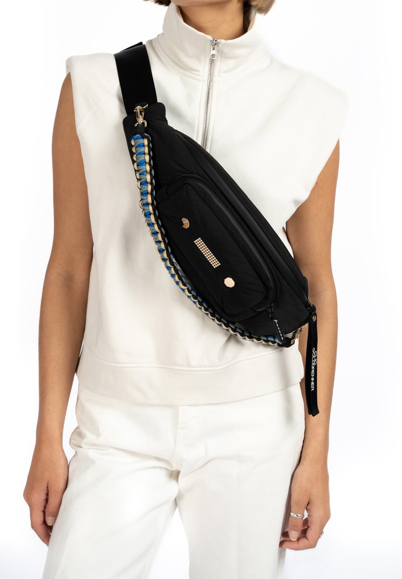 Zwarte schoudertas met een gevlochten blauw en tan schouderband, voorzien van een ritsvak, metalen accenten en een sleek ontwerp. Gewatteerde stof.