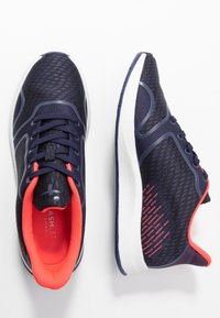 Námořnické sportovní boty s síťovaným svrškem, bílou podešví a živými červenými akcenty na obvodu a patě. Obsahují strukturální vzor po celém povrchu.