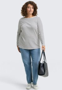 Gestreiftes Langarmoberteil in Weiß und Schwarz, kombiniert mit hellblauen Jeans. Die Accessoires umfassen eine schwarze Handtasche und weiße Sneakers.
