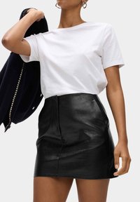 Černá kožená mini sukně s předním švem a obepínajícím střihem, v kombinaci s obyčejným bílým bavlněným tričkem a námořnickým kardiganem.