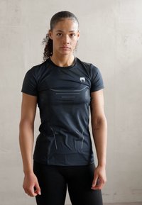 Svart treningst-skjorte med korte ermer, strukturerte mønstre, reflekterende detaljer og en tettsittende design. Brukt sammen med svarte leggings.