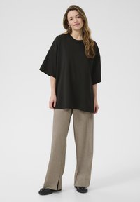Sort oversized t-shirt med korte ærmer, parret med lysebrune vidde bukser med sideslids, og sorte chunky sko.