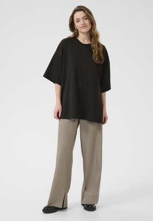T-shirt noir surdimensionné à manches courtes, associé à un pantalon large marron clair avec des fentes sur les côtés, et des chaussures noires épaisses.