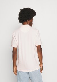 Polo skjorte i lys rosa bomull med klassisk krage, korte ermer og rett falm. Har et subtilt design med bakstykke.