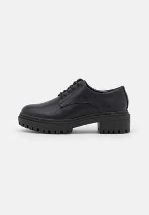 Chaussure en cuir noir avec un bout arrondi, un laçage, une semelle en caoutchouc épaisse avec des détails de traction, et un petit talon carré.