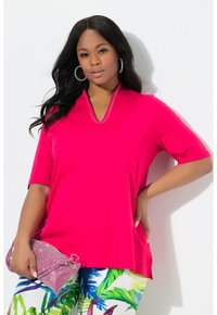 Fuchsia kortelumige top met een V-hals en decoratieve studs. Gecombineerd met bloemenpatroon broek en een sprankelende clutch.
