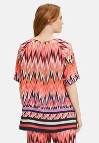 Haut à motif zigzag coloré présentant des teintes de rose, d'orange et de noir, avec une coupe ample et des manches courtes. Large bande horizontale au bas.