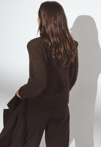 Brūns teksturēts džemperis ar apaļu kakla izgriezumu un garām piedurknēm, apvienots ar tumšām biksēm. Audums izskatās silts un patīkams.