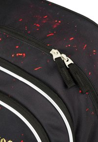 Černý batoh s tečkovaným červeným vzorem, s dvěma zipy a bílými akcenty na bocích. Vyrobeno z odolné tkaniny.
