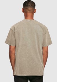 Camiseta de manga corta en color beige claro con un acabado suave y texturizado y un clásico cuello redondo; espalda lisa sin gráficos ni adornos.