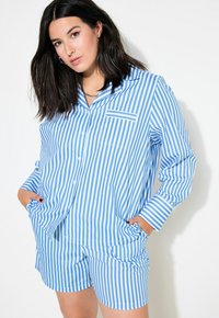 Conjunto de pijama a rayas azules y blancas que incluye una camisa de botones con un bolsillo y pantalones cortos. La tela tiene una textura suave y un corte relajado.