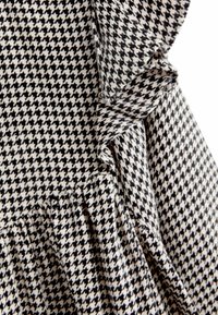 Tissu à motif pied-de-poule noir et blanc avec des bords festonnés, mettant en avant un tissage texturé et des blocs de couleurs contrastants.