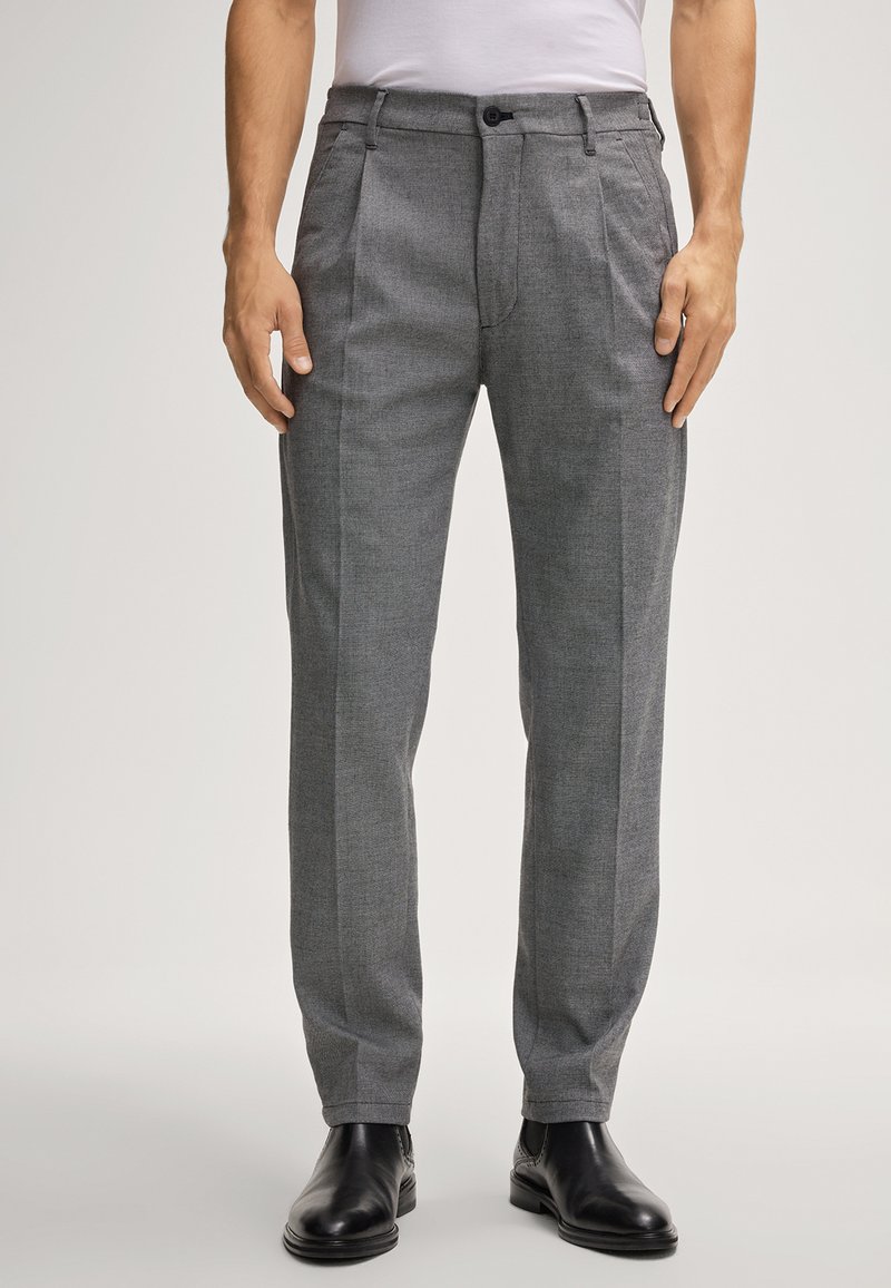 Grijze op maat gemaakte broek met een gladde textuur, voorzien van een knoopsluiting en voorbenen, gedragen met zwarte leren schoenen.