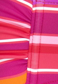 Daugiakampė juostuota medžiaga, kurios atspalviai svyruoja nuo rožinės iki oranžinės ir baltos. Paviršius yra banguotas, su raukiniais palei siūlę.