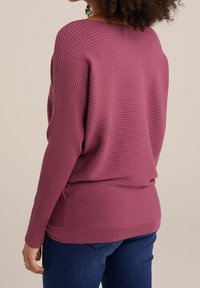 Pitkähihaisessa, ribattu neulepaidassa tummanpunainen sävy. Ominaisuuksiin kuuluu rento fit ja pyöreä kaula-aukko. Yhdistettynä sinisiin farkkuihin, mikä luo rennon ilmeen.