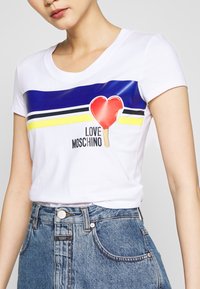 Bílý tričko s kulatým výstřihem, s modrou pruhovanou a barevným obrázkem zmrzliny ve tvaru srdce. V kombinaci s džínovými šortkami.