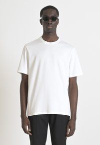 T-shirt bianca a maniche corte, con scollo rotondo, realizzata in morbido cotone, con un piccolo logo stampato in un colore chiaro sul petto.