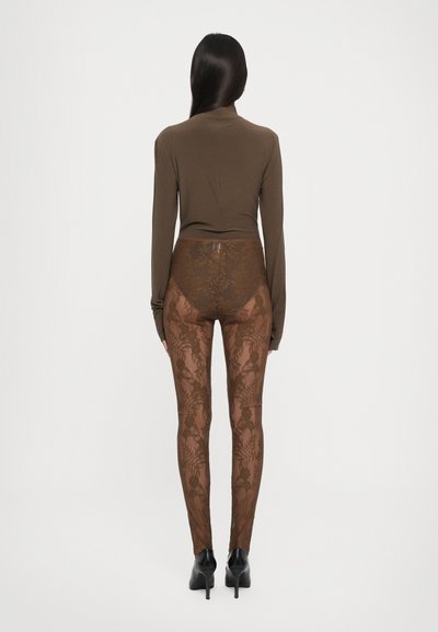 Brun langermet topp kombinert med gjennomsiktige brune leggings med blomstermønster, båret med svarte høye hæler, sett bakfra.