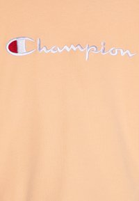 Őszibarack színű pamut póló, fehér hímzett "Champion" logos megjelenéssel, piros kiemeléssel. Puha tapintás és klasszikus szabás.