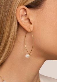 Pendiente de aro dorado con forma alargada, adornado con una perla blanca. Acabado metálico suave con un diseño minimalista.