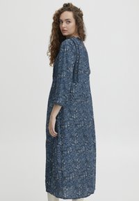 Lungo vestito blu con motivo floreale, maniche a tre quarti e tessuto testurizzato. Presenta una chiusura legata sul retro.