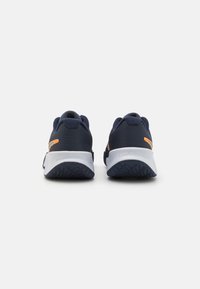 Marineblå atletik sko med tekstureret stofoverdel, orange accent og hvid sål; rund hæl og gripmønster på gummisålen.