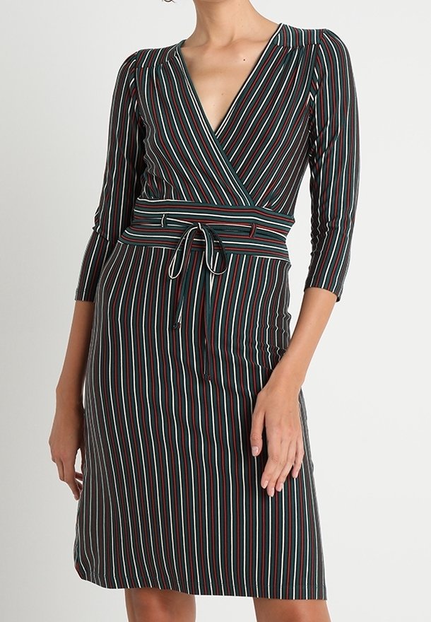 Femme portant une robe portefeuille ajustée longueur genoux avec des rayures verticales noires, blanches, rouges et vertes et des manches trois-quarts.