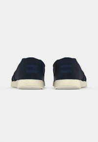 Meripihkaiset liukukengät, joissa on tekstuuripinta, vaaleanbeige kumipohja ja TOMS-logo näkyvissä kantapäässä.