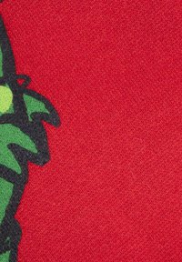 Tessuto rosso con superficie texturizzata e un motivo verde, mostrato parzialmente, mettendo in risalto contorni neri e un contrasto di colori vivaci.