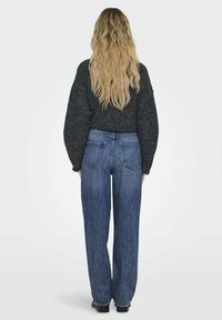 Pulover din tricot supradimensionat, de culoare gri închis, purtat cu blugi largi, de culoare albastră. Blugii au cinci buzunare și un croi la mijlocul taliei.