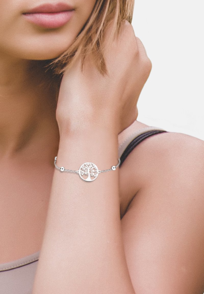 Silberarmband mit einem kreisförmigen Baumdesign, zarter Kette und runden Akzenten, am Handgelenk getragen. Glatte Metalloberfläche.