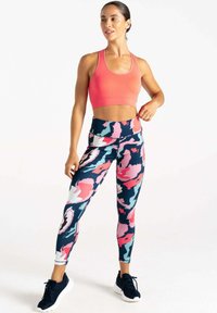 Rosa Sport-BH mit strukturiertem Muster, kombiniert mit bunten Leggings mit einem abstrakten Camouflage-Muster in Dunkelblau, Pink und Hellblau. Schwarze Sneaker.
