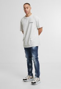 Šedé bavlněné tričko s krátkým rukávem, spárované s modrými ošoupanými džíny a bílými teniskami s černými a béžovými akcenty.