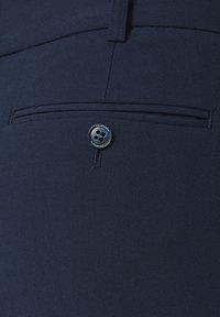 Granatowe spodnie z płaską kieszenią z zamknięciem na srebrny guzik, gładką teksturą i szczegółami dostosowanymi do sylwetki.